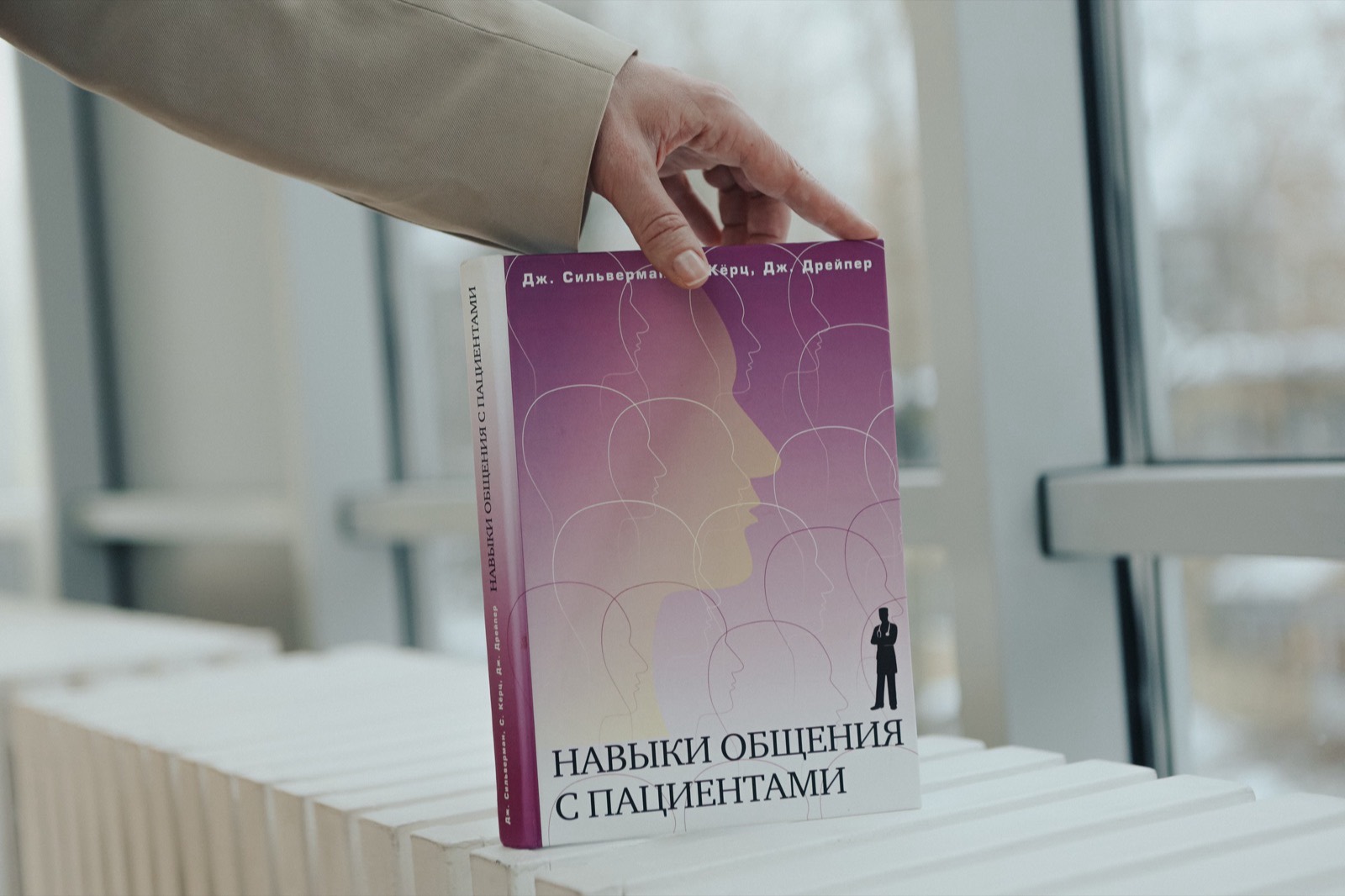 Книга «Навыки общения с пациентами» Сильвермана, Кёрц и Дрейпер в руке на фоне окна